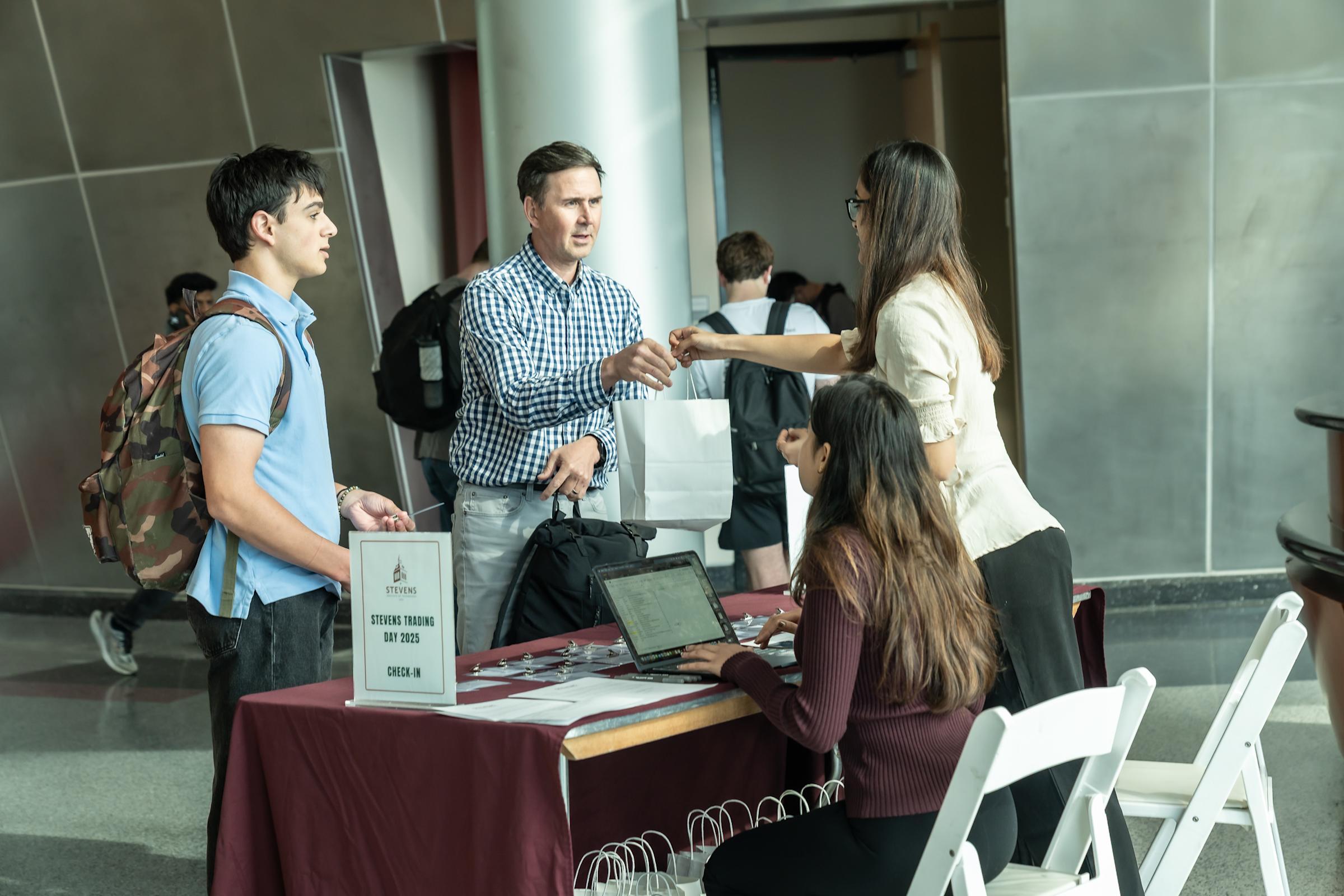 A man and son receive registration materials at the check in desk inside the Babbio Center Atrium.