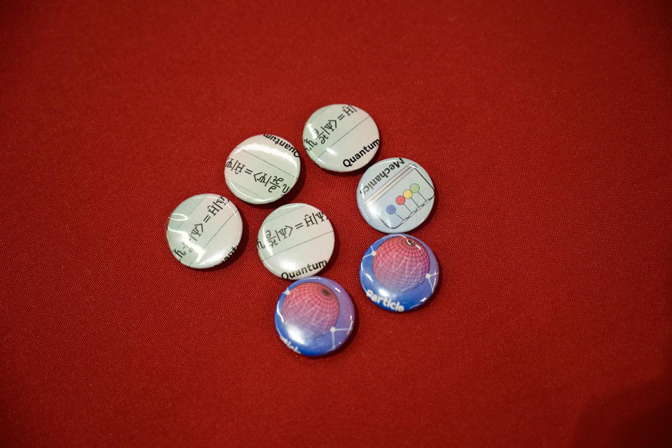  A set of custom buttons designed for the 2025 CUWIP at Stevens on a red table.