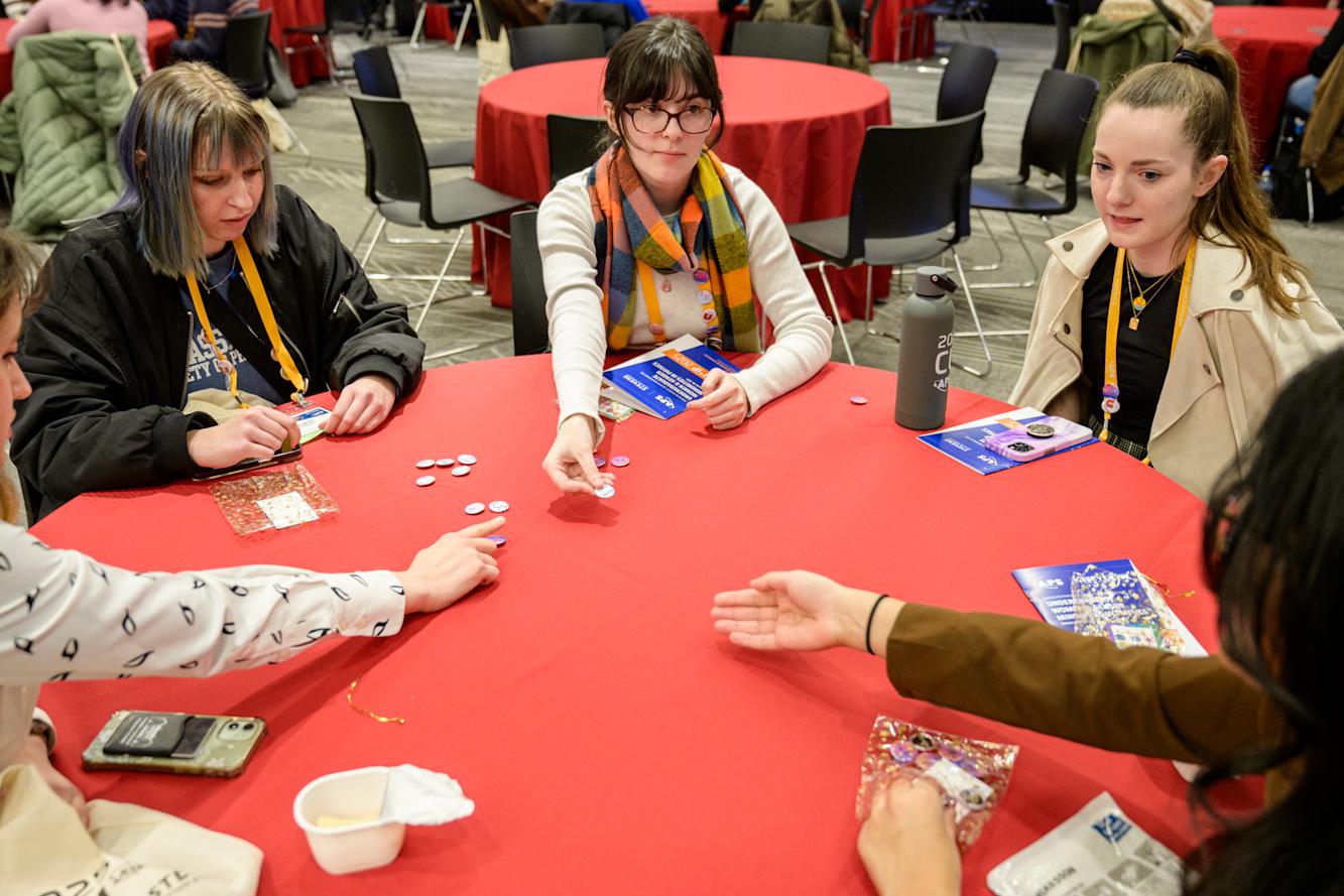 A group of students sitting at a red round table trading buttons at the 2025 CUWIP event.