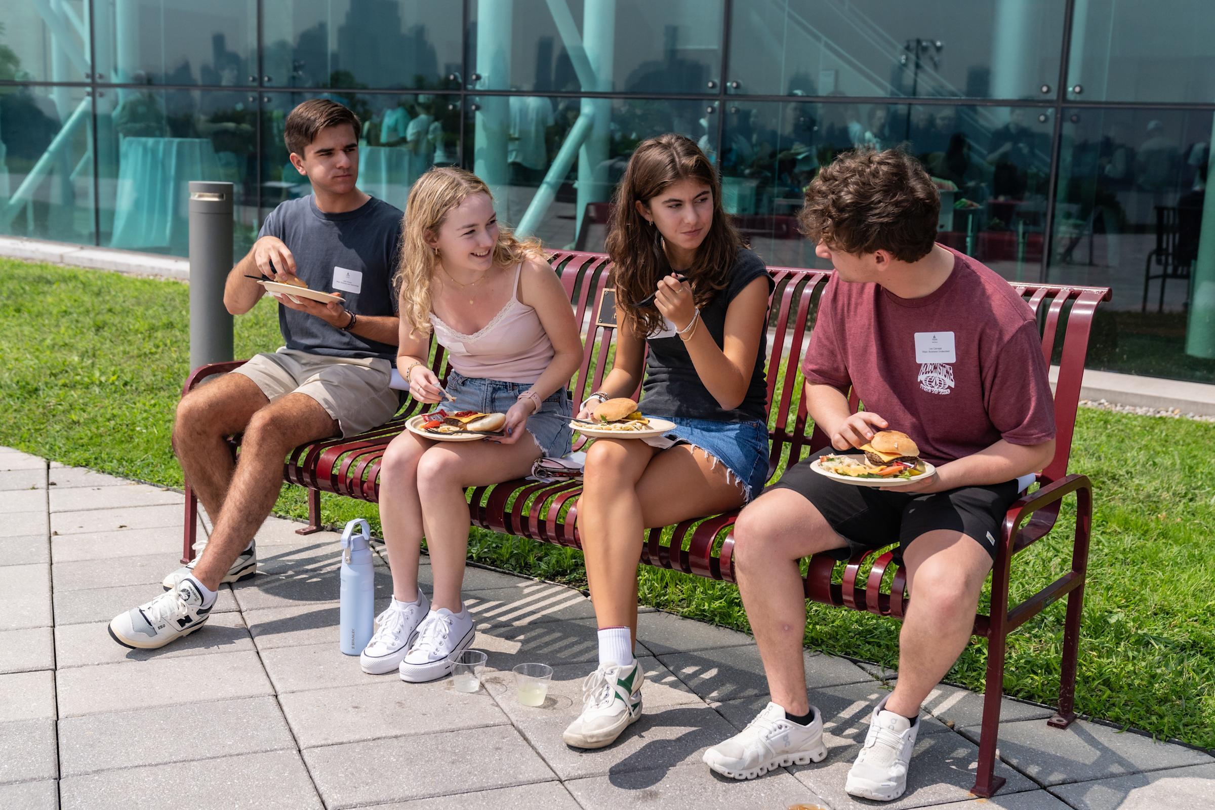 Students sit on a bench eating lunch on the Babbio patio.