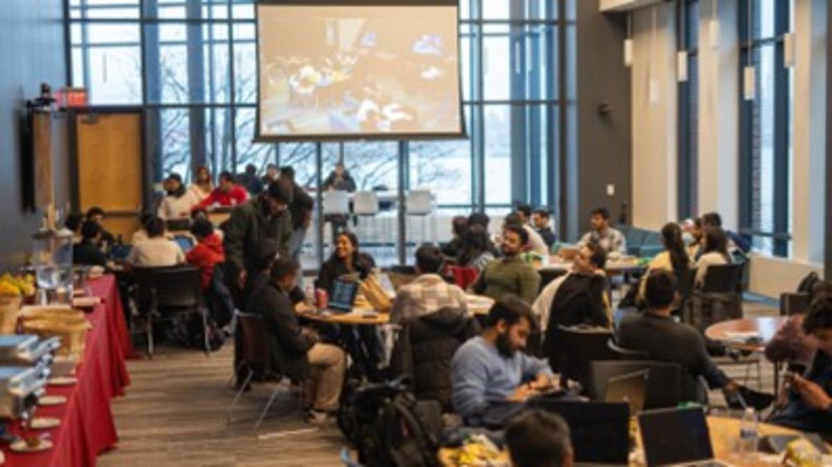 A room full of students sitting with their laptops and lunches. There is a long table of catered food on the left.