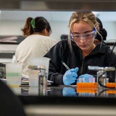 Student in a lab wearing safety goggles and writing notes.