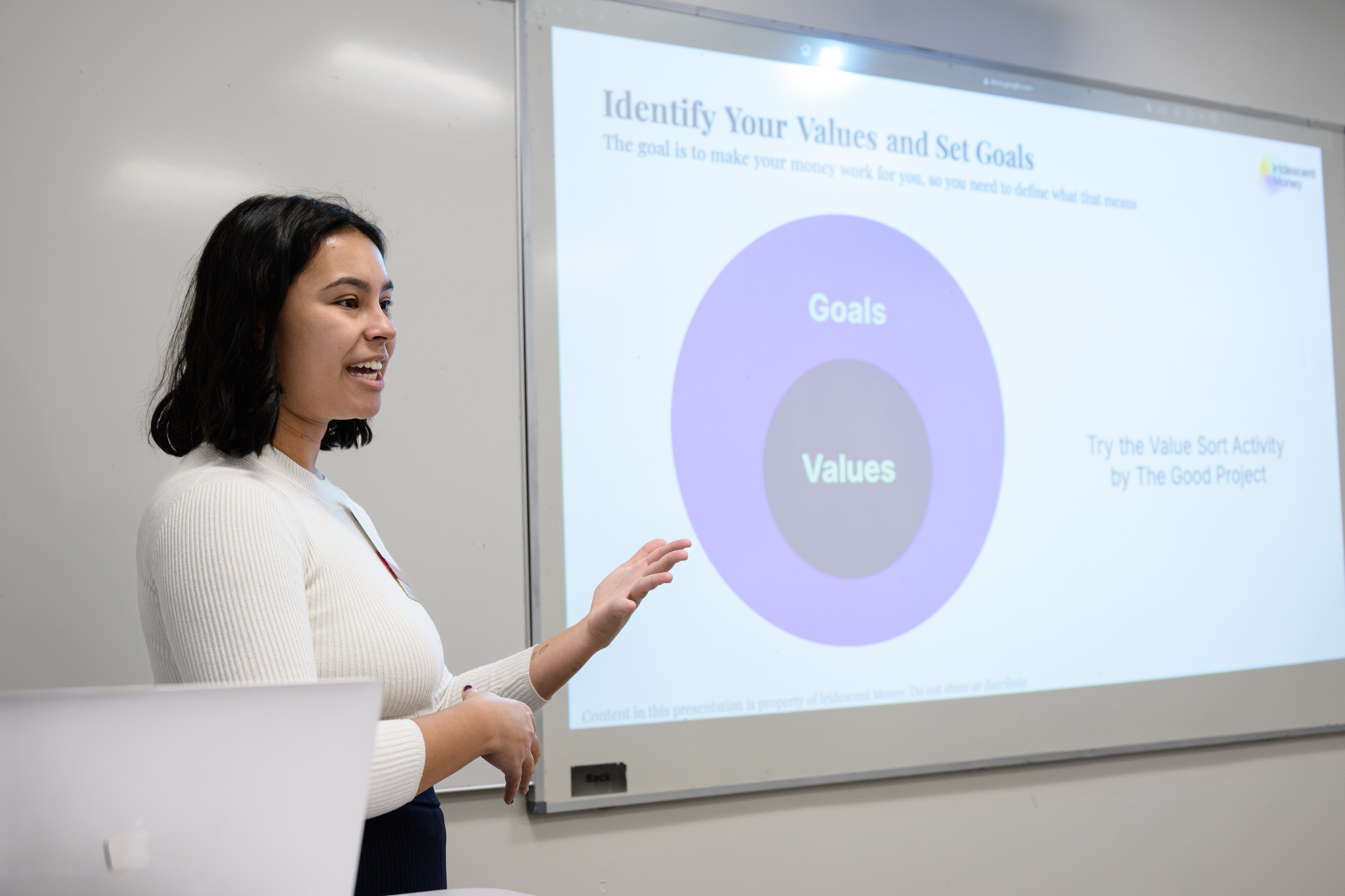 Mia Vellon stands in front of a room giving a presentation on personal finance