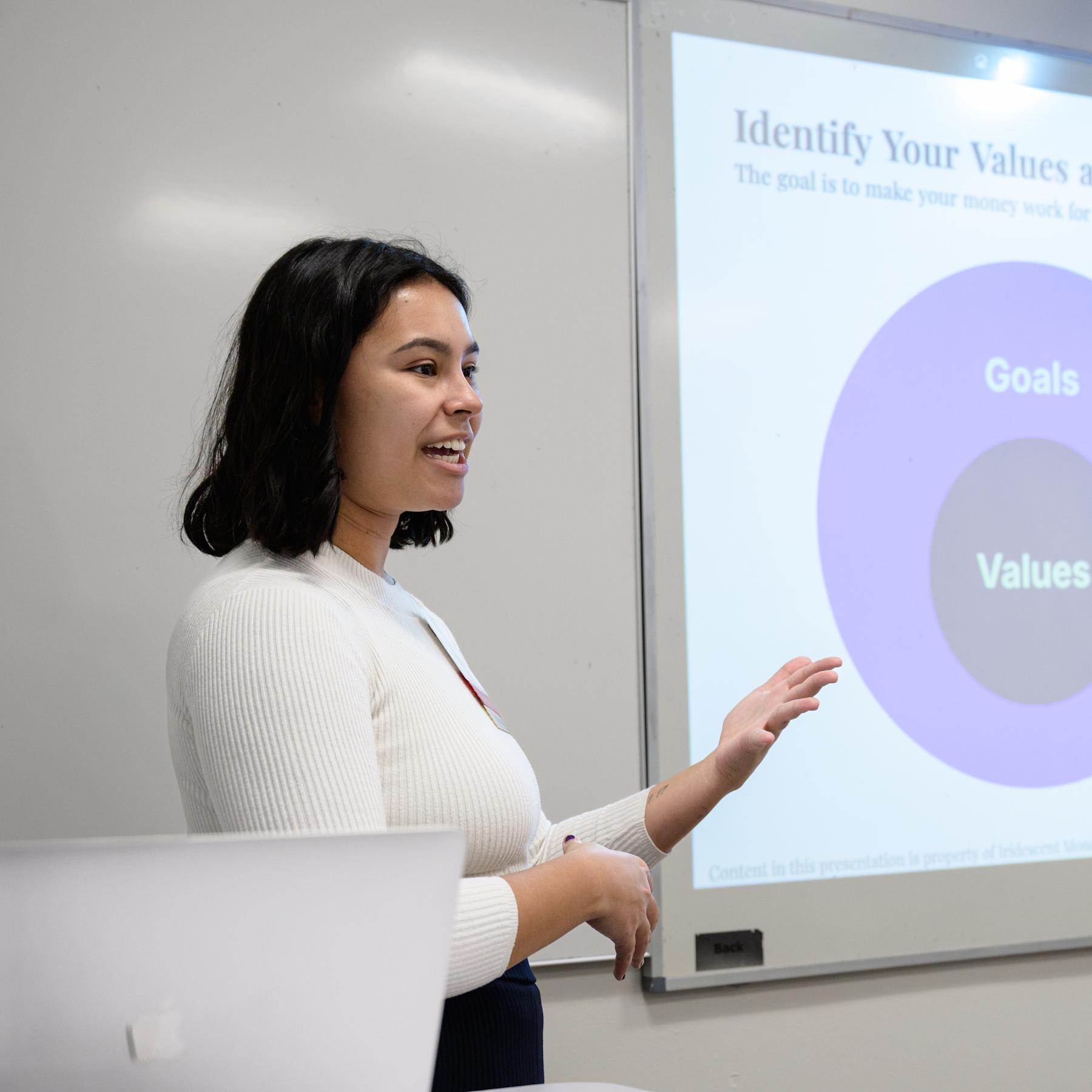 Mia Vellon stands in front of a room giving a presentation on personal finance
