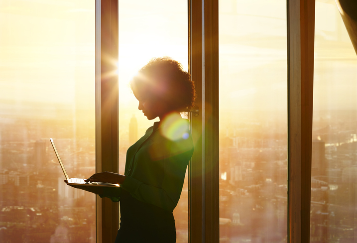 Businesswoman looking at laptop standing by window