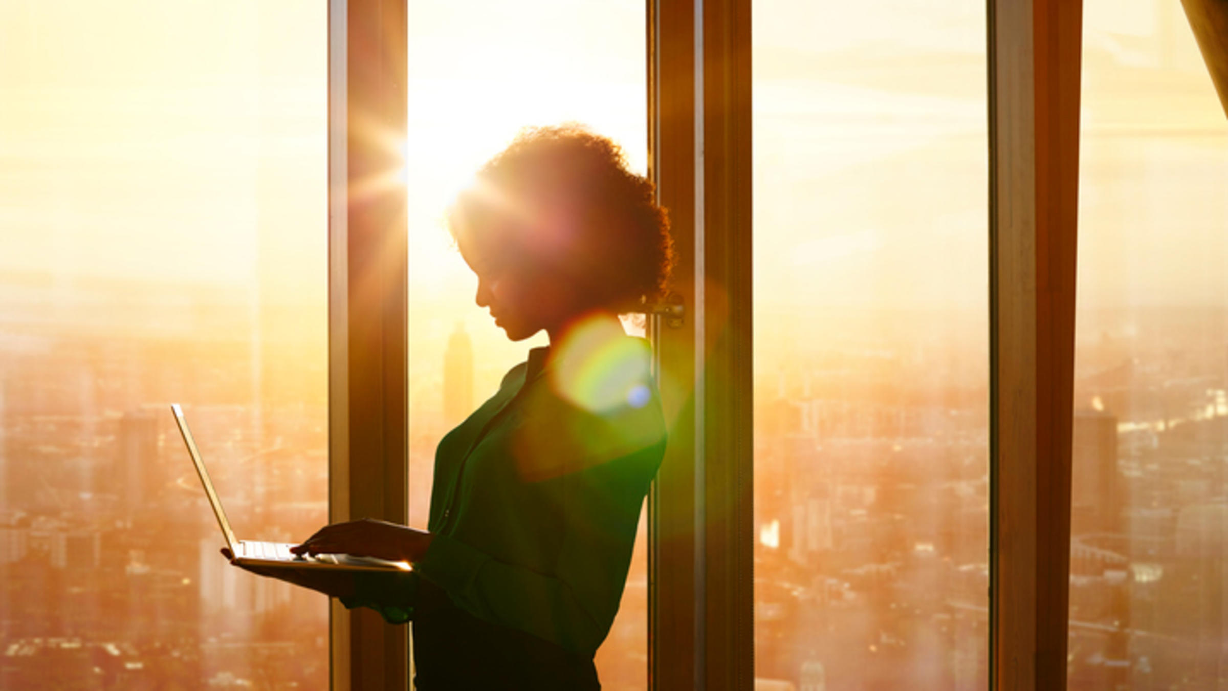 Businesswoman looking at laptop standing by window