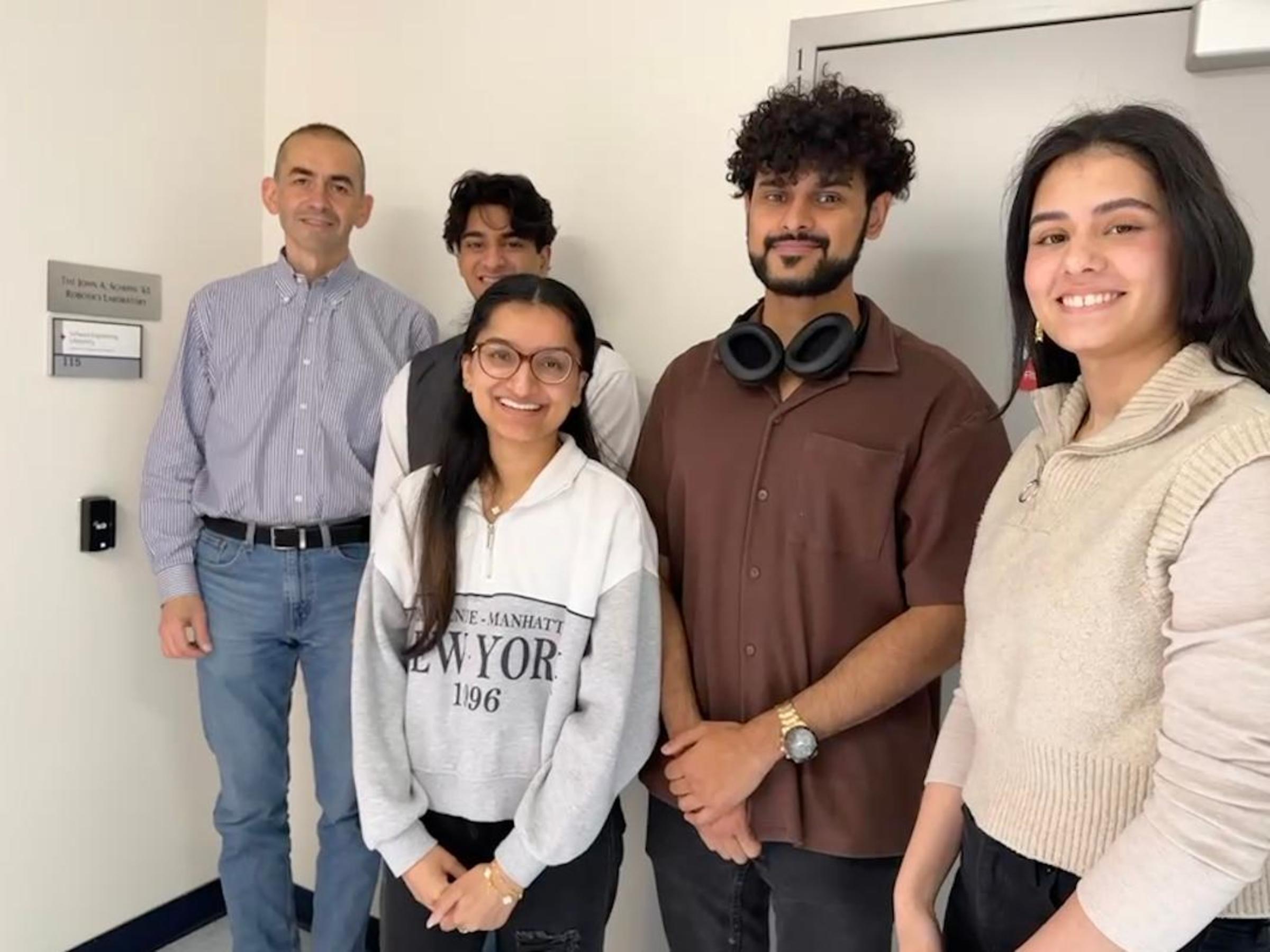 Four students and their advisor stand in front of a door.