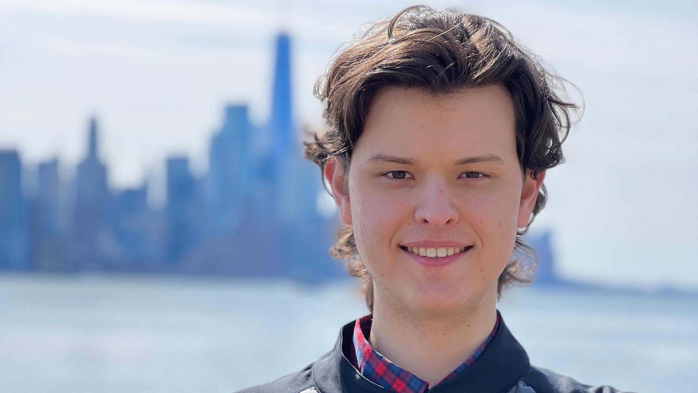 Graduate student Adam Leszczynski smiling on Stevens' campus with New York City in the background.