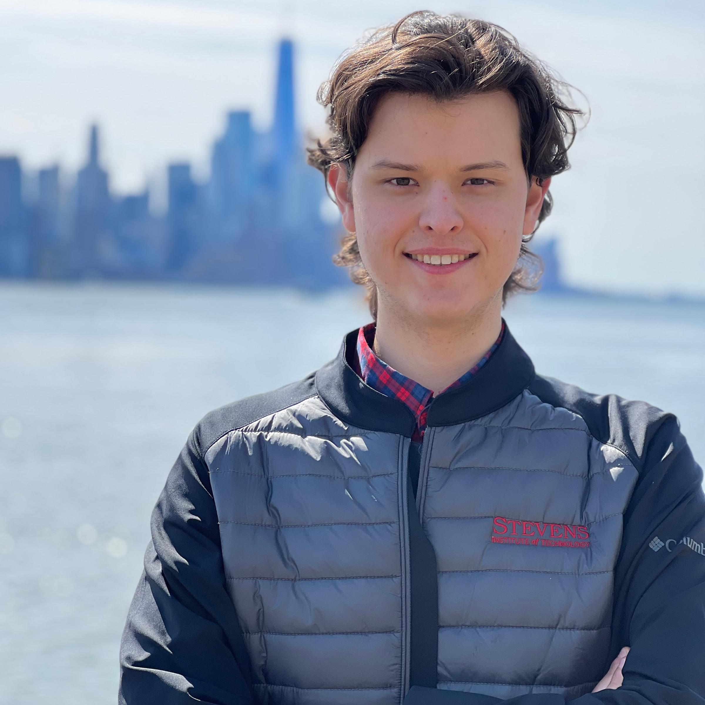 Graduate student Adam Leszczynski smiling on Stevens' campus with New York City in the background.