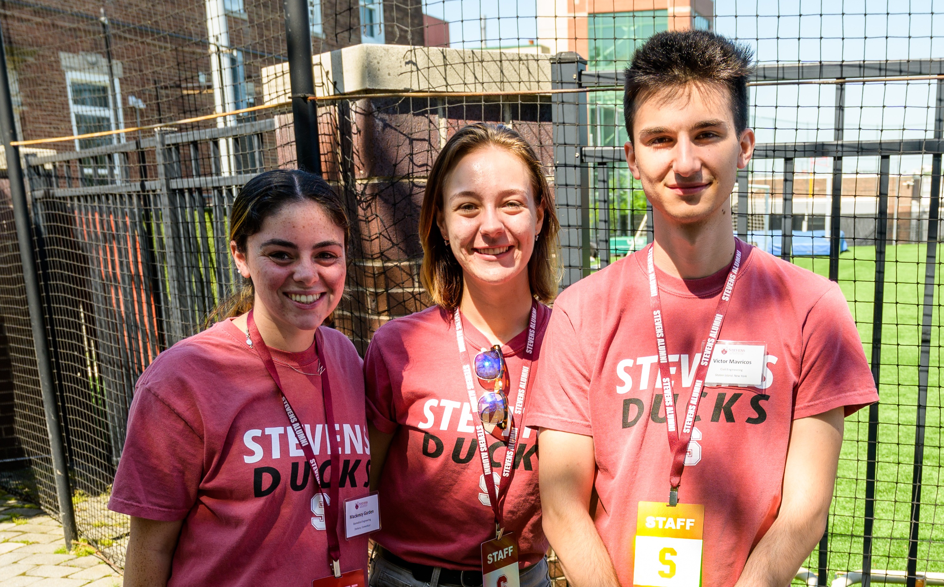 Three students smile at a table on campus with Stevens Ducks shirts on