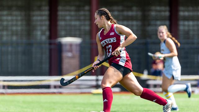Field hockey player runs up the field with the ball