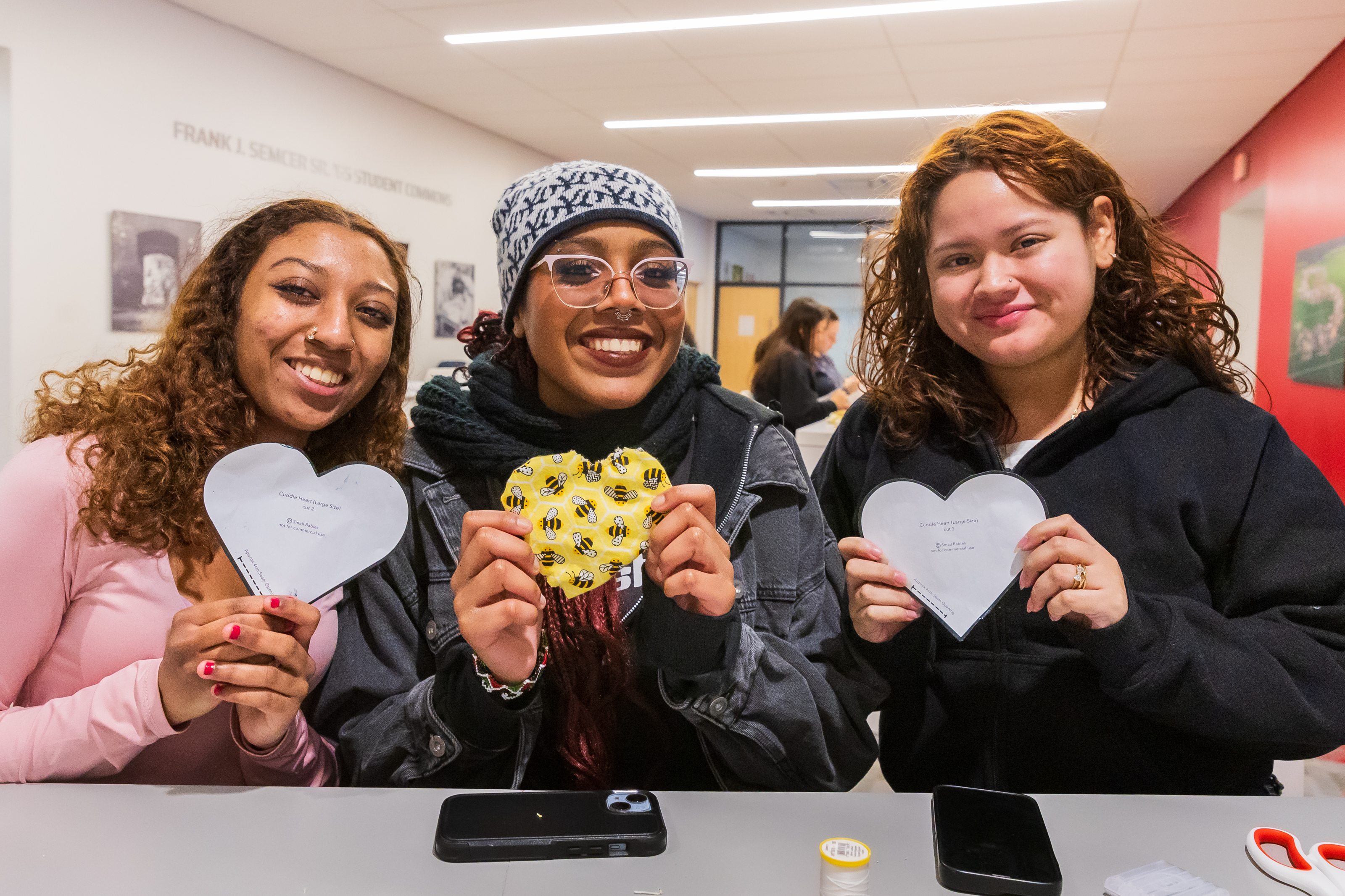Three students holding "Cuddle Heart" patterns as part of a service project for MLK Week of Service. The students smile together, embodying unity and community involvement.