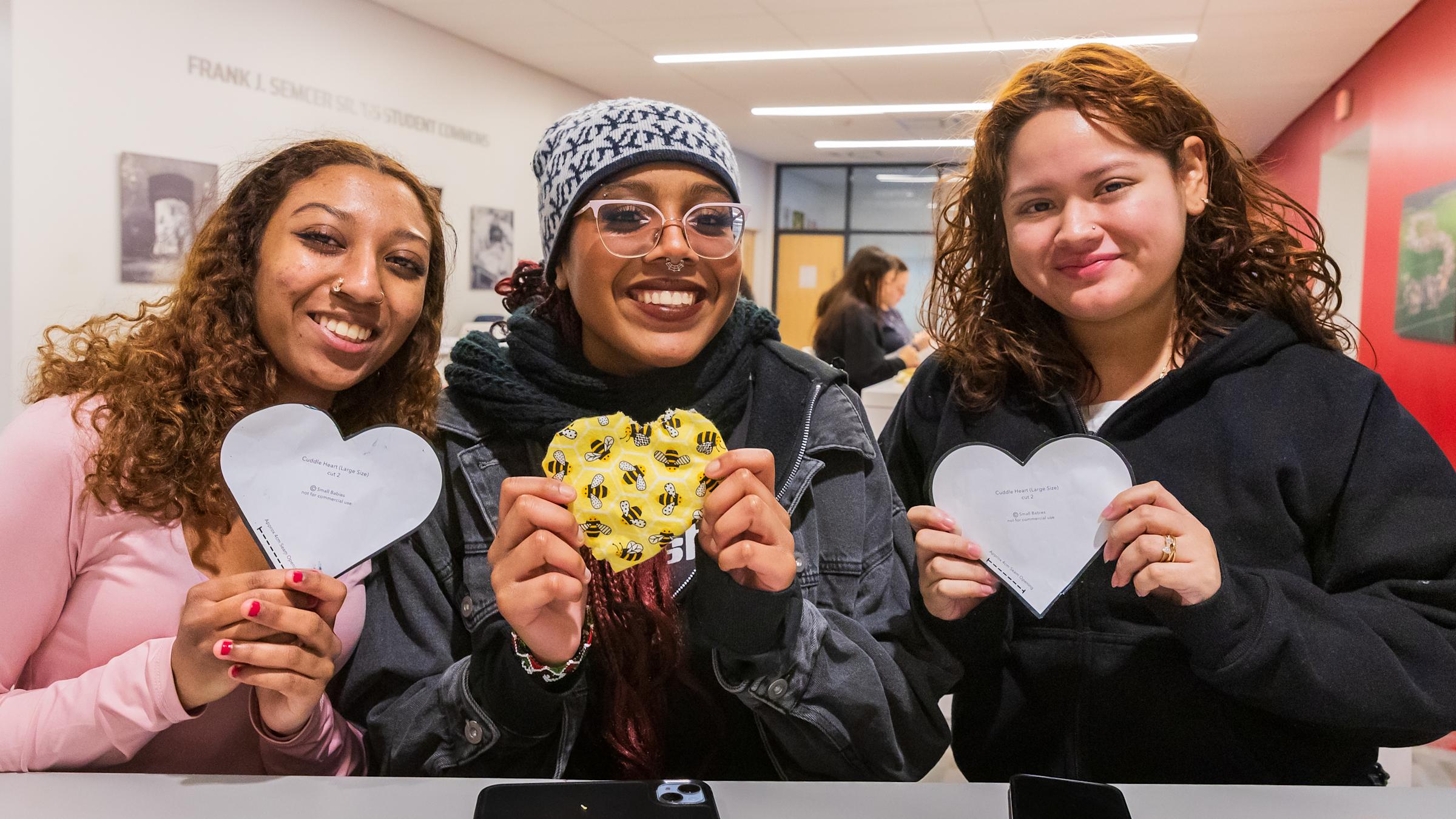 Three students holding "Cuddle Heart" patterns as part of a service project for MLK Week of Service. The students smile together, embodying unity and community involvement.