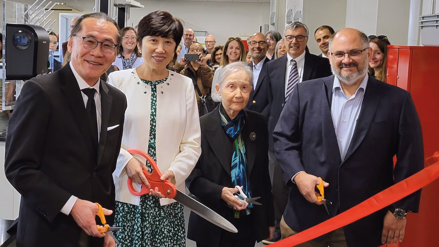 Photo of four people cutting a ribbon, with about 12 people standing behind them.