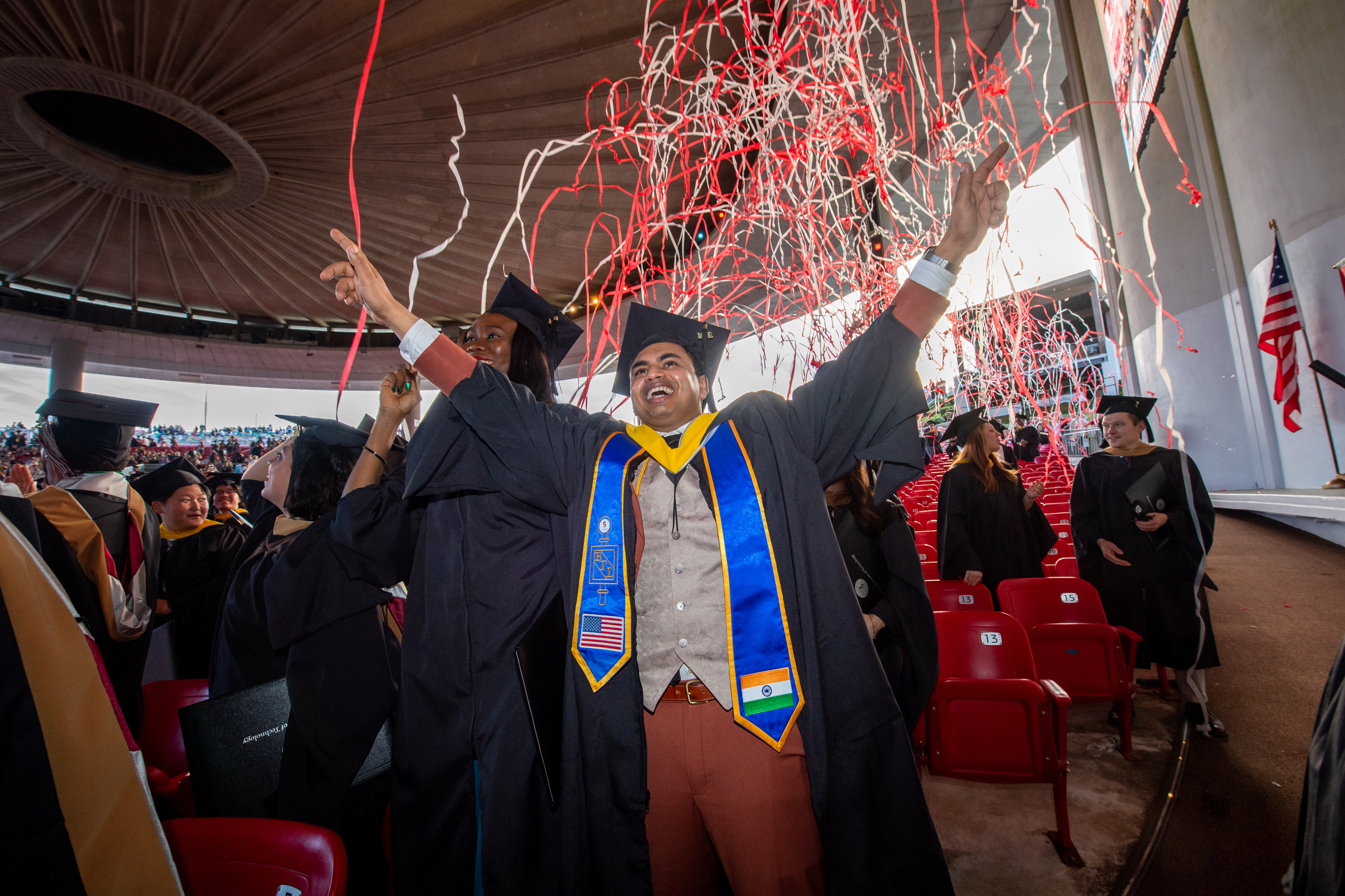 A graduate student celebrates his Commencement under a streams of read and gray confetti.