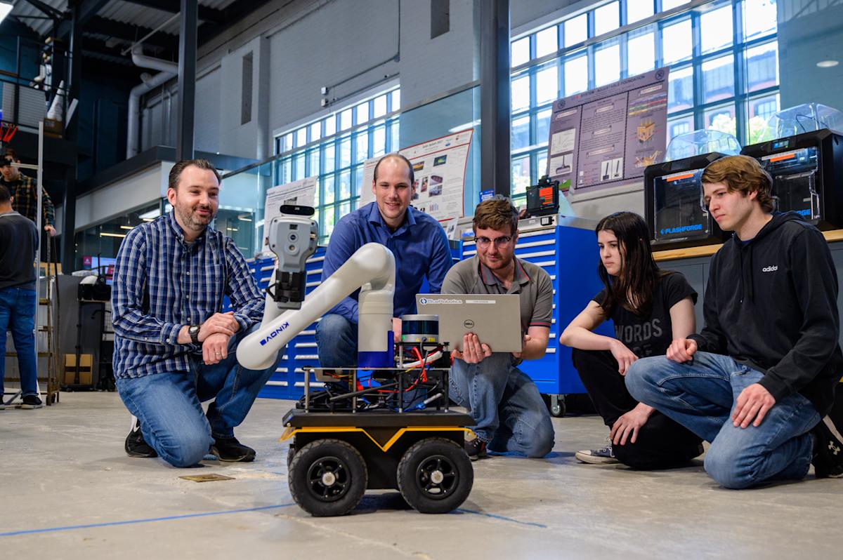 Individuals gather on a lab floor around a robot