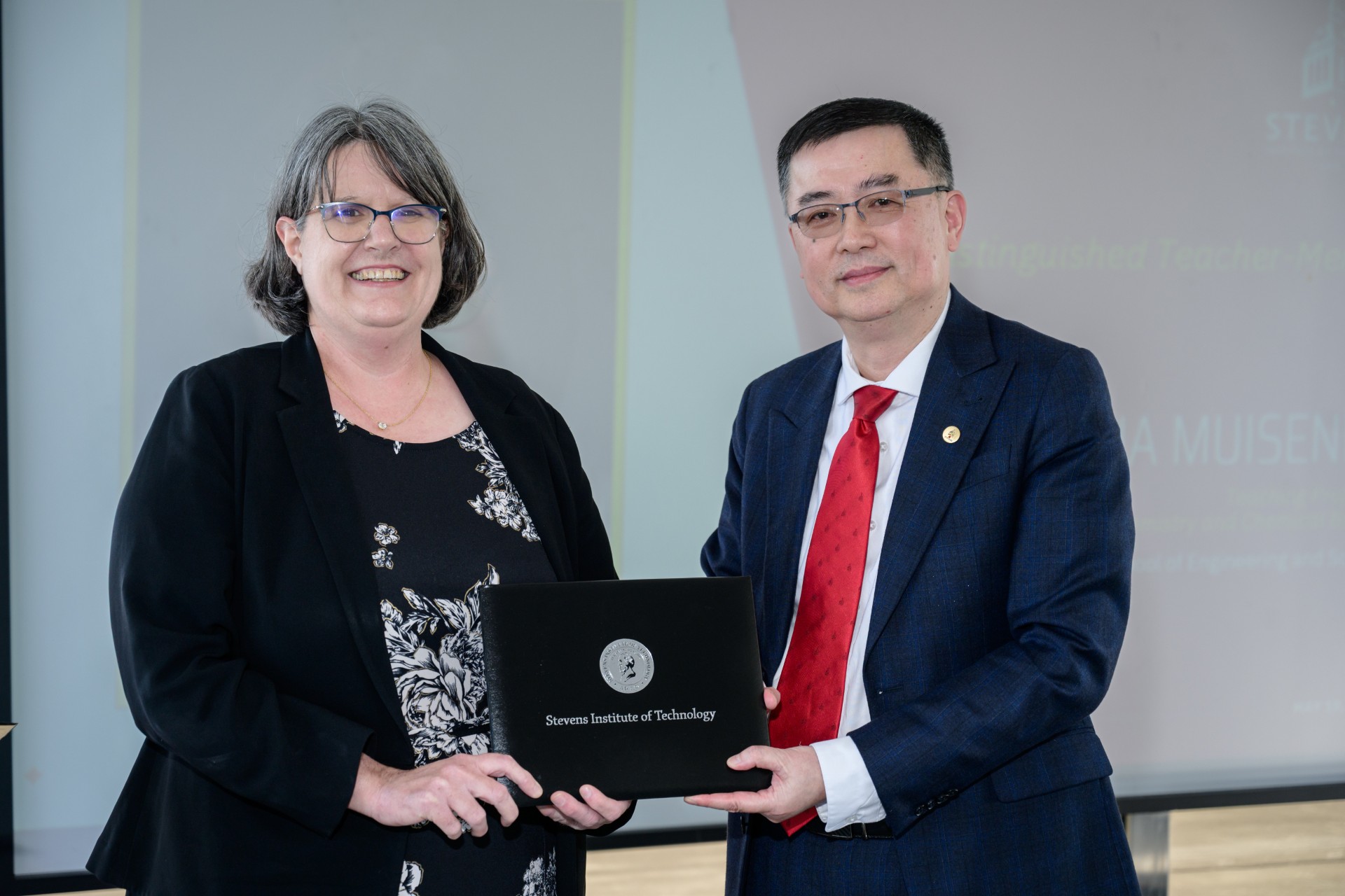 A waist-up shot of Jianmin Qu, Patricia Muisener, Nariman Farvardin standing next to each other. Patricia is holding an award.