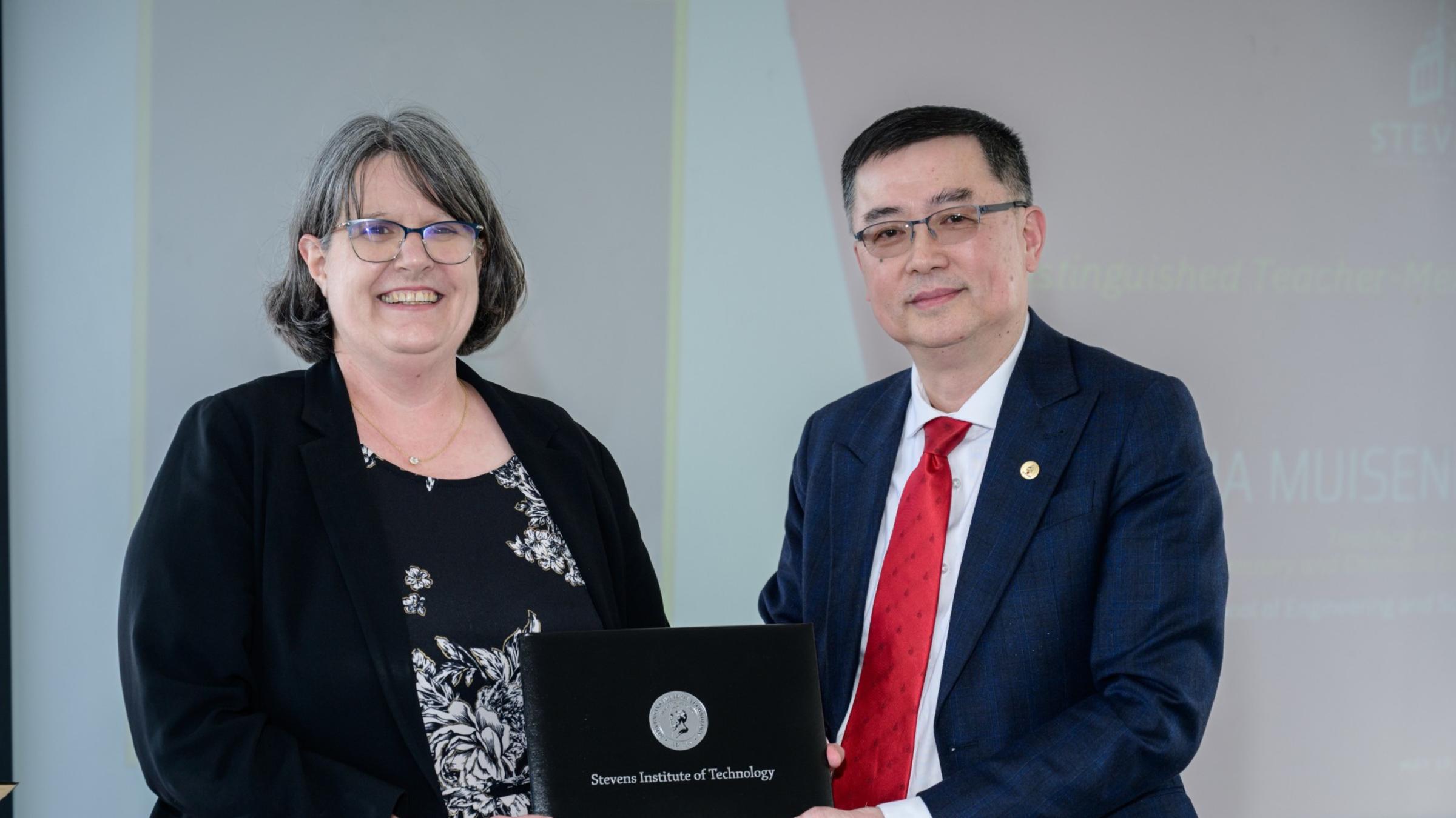 A waist-up shot of Jianmin Qu, Patricia Muisener, Nariman Farvardin standing next to each other. Patricia is holding an award.
