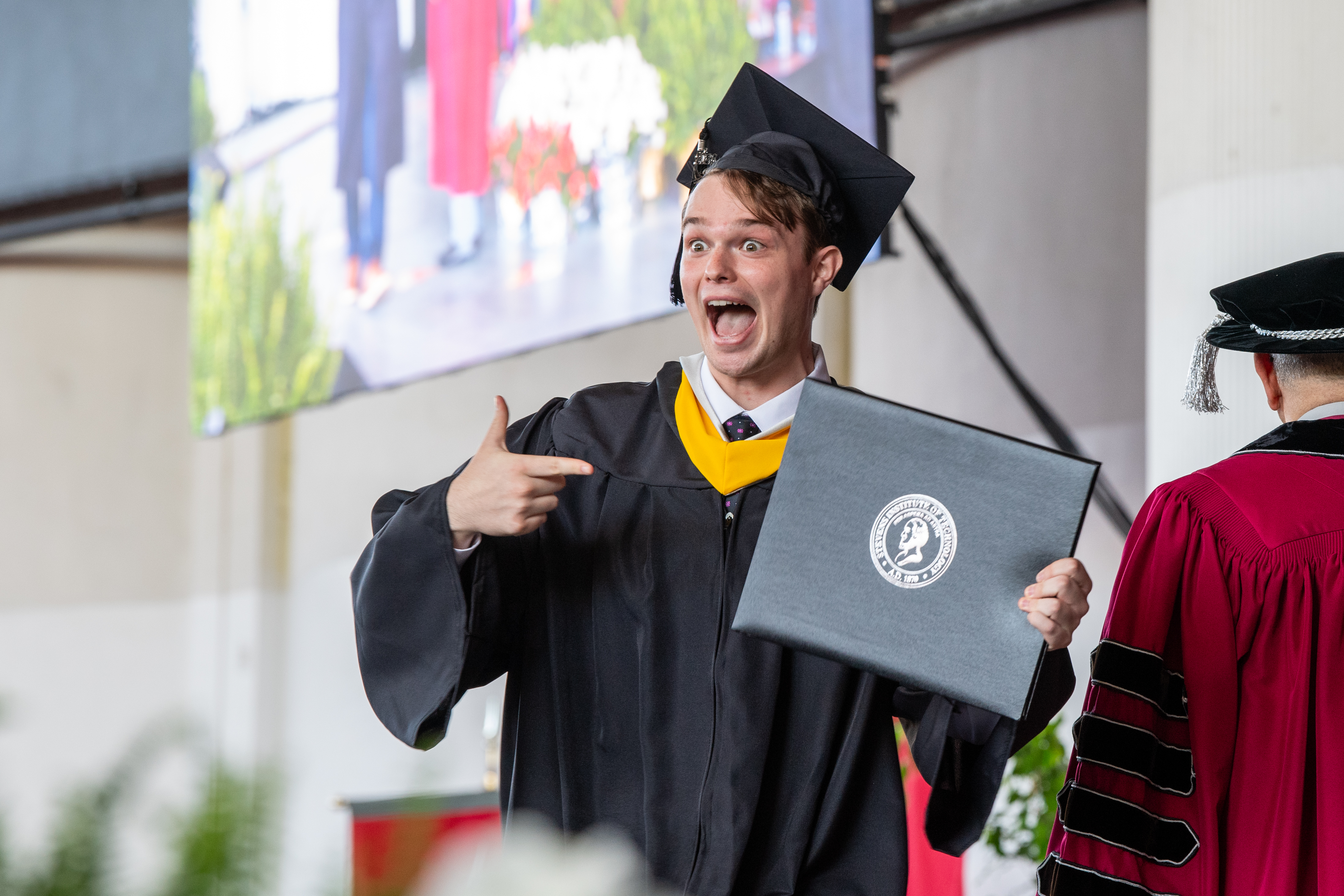 An excited student at Commencement receives his diploma