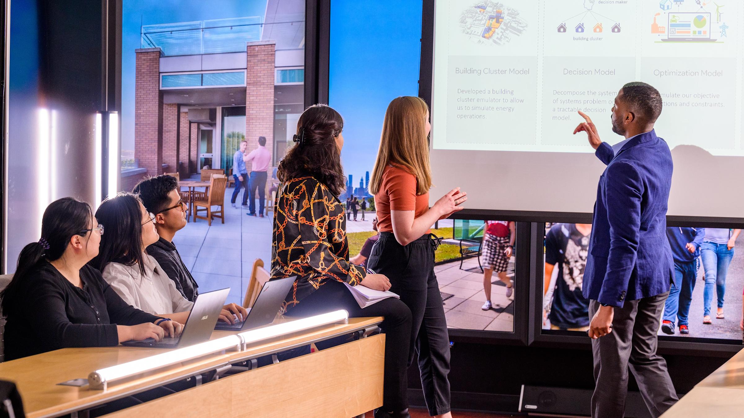 Students and a faculty member review information on a presentation screen in the immersion laboratory.