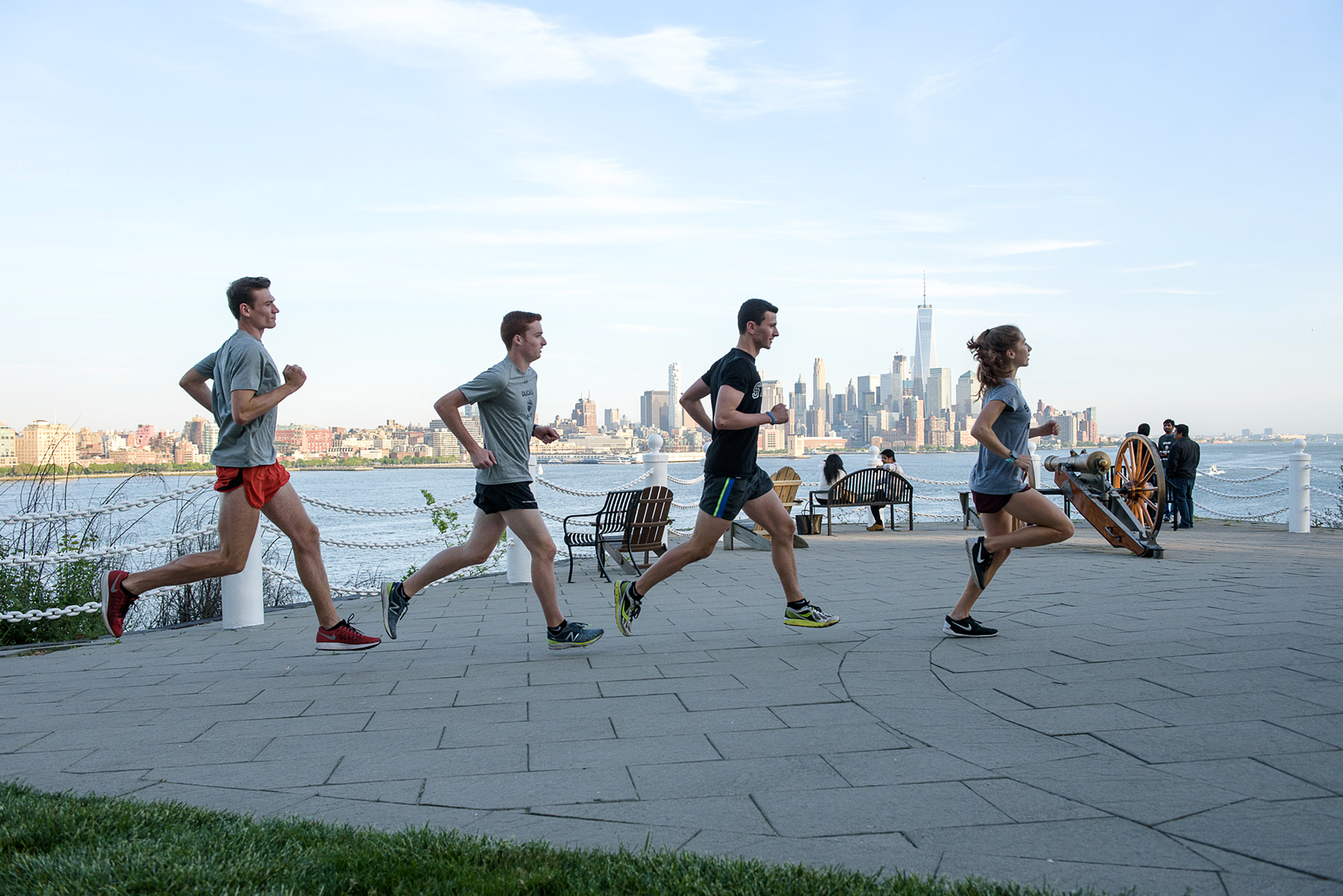 Group of four runners jog past Castle Point Terrace with New York skyline in background.