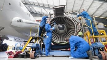 A group of engineers in blue suits work on a jet engine turbine.