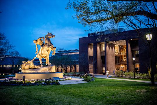 Campus view with Torch Bearers sculpture and Library in background, taken at dusk.