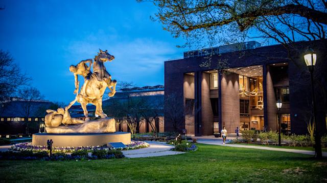 Campus view with Torch Bearers sculpture and Library in background, taken at dusk.