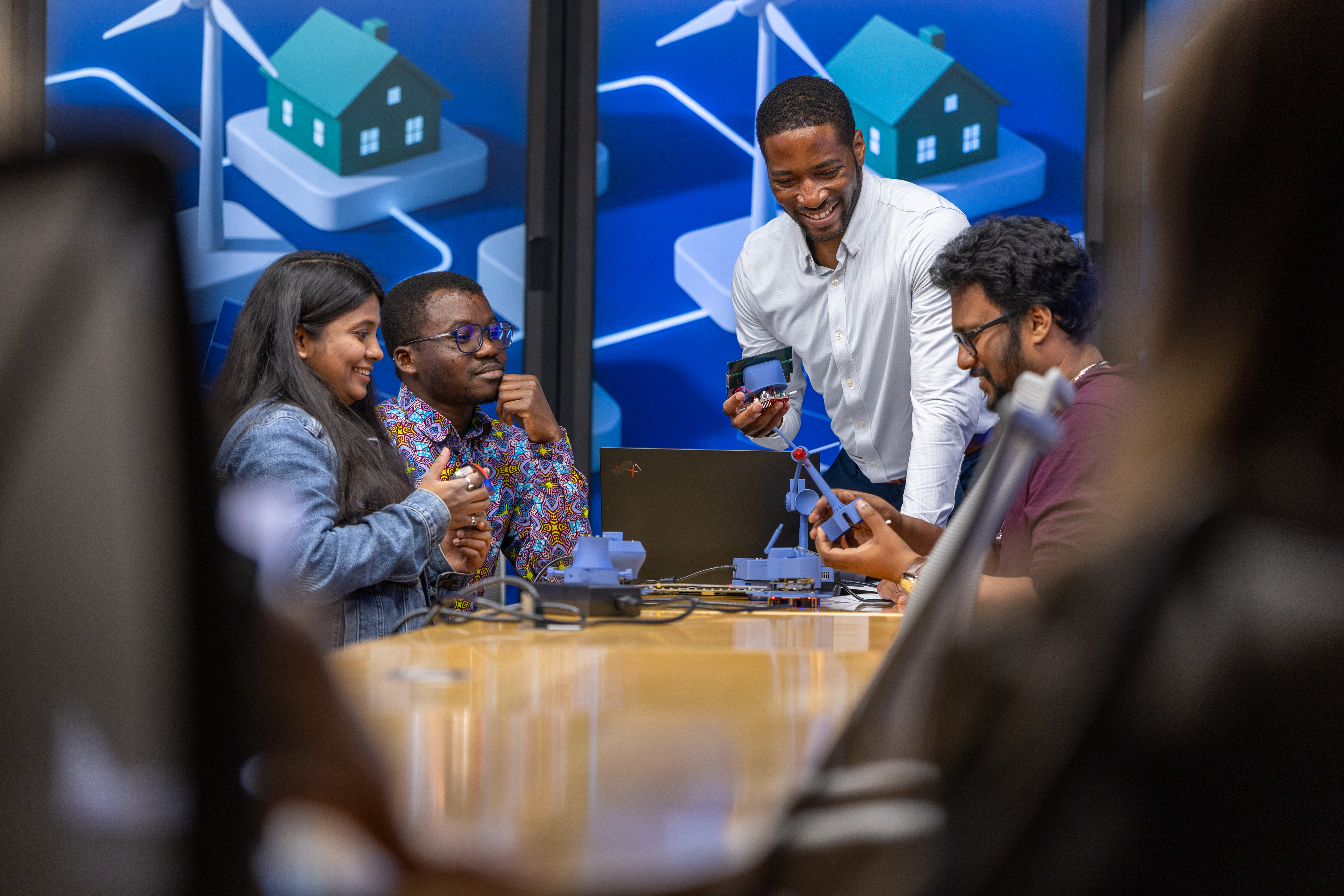 Professor Philip Odonkor smiling with three students while working with modeling in front of a wall of monitors. 