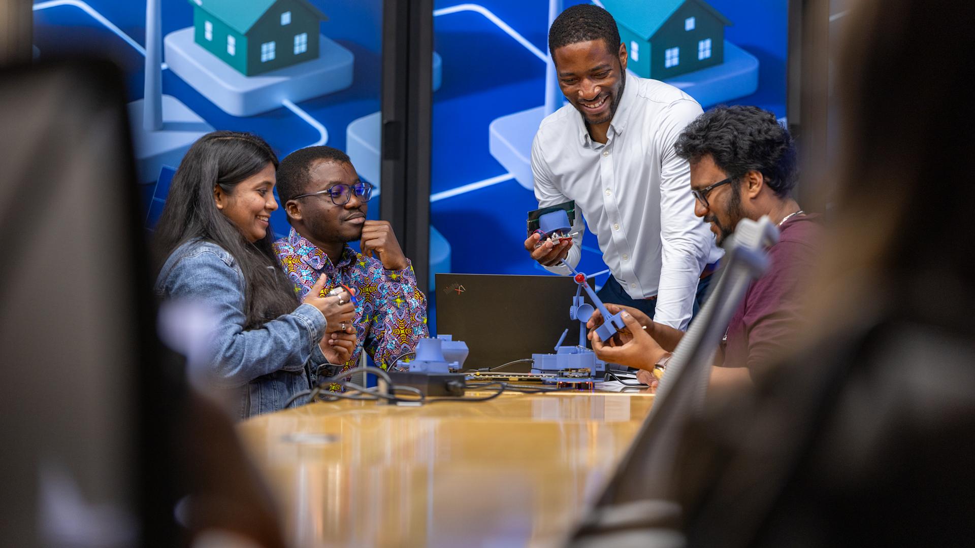 Professor Philip Odonkor smiling with three students while working with modeling in front of a wall of monitors.