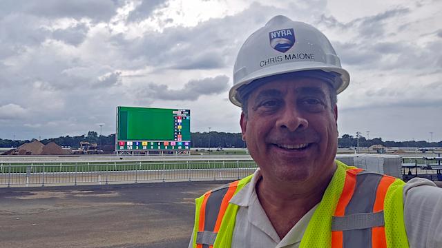 Maione at Belmont Park racetrack in construction hat and vest, with its six-story Infield LED video board that he helped bring to life in the background.