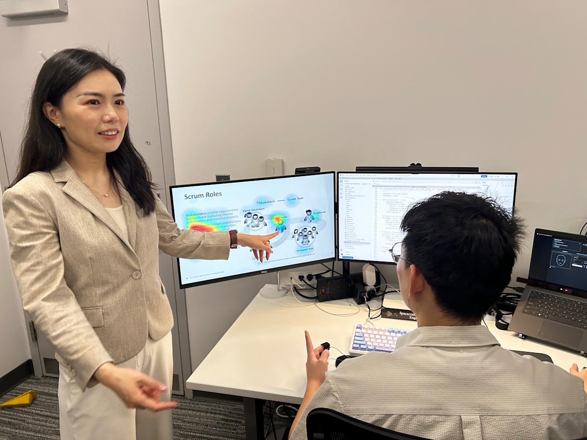 Ting Liao standing to the left of one of her ph.d. students who is sitting at the computer where she is pointing and explaining what is on the screen.