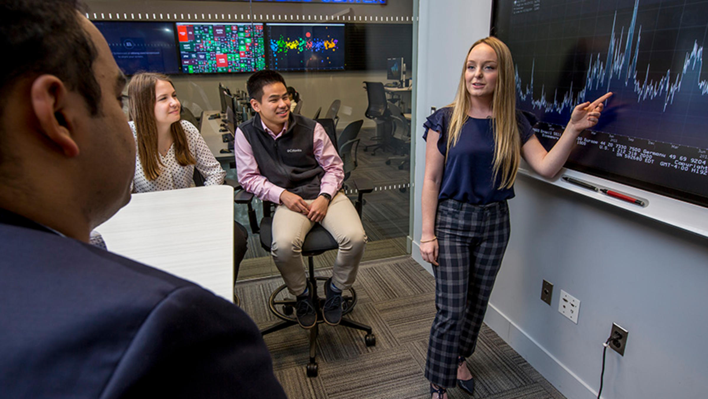 A female student works a smart board as they lead a class discussion about investing amid volatility.