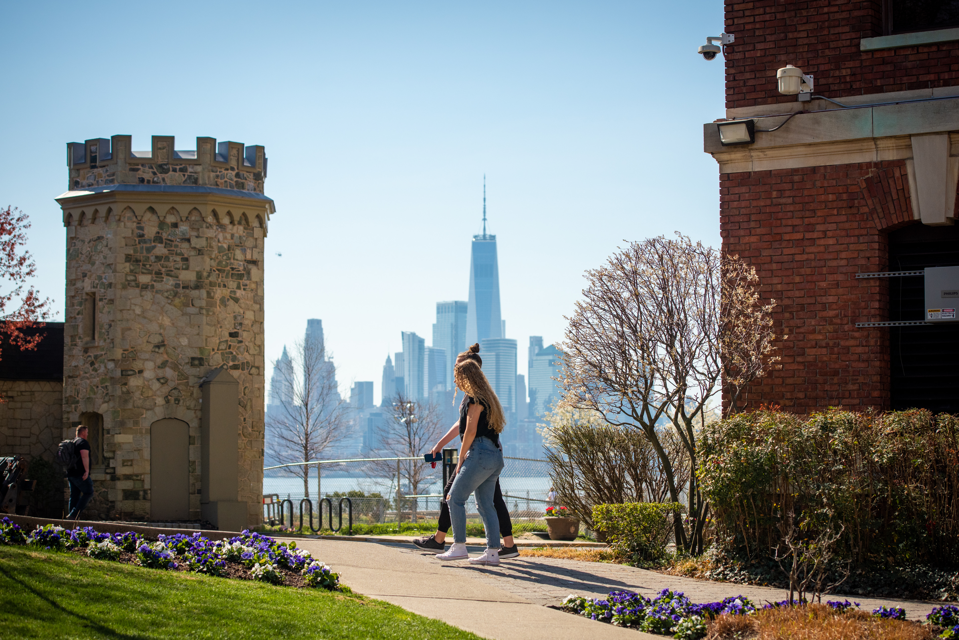 Students walk across campus next to Gatehouse with WTC and downtown Manhattan in background.