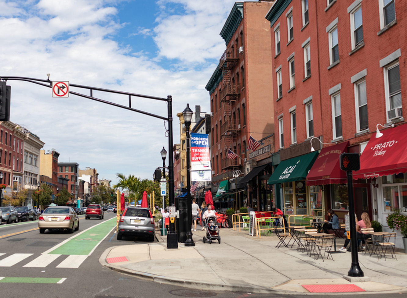 Downtown Hoboken on a partly sunny day. People our eating outside and walking down the sidewalks. 