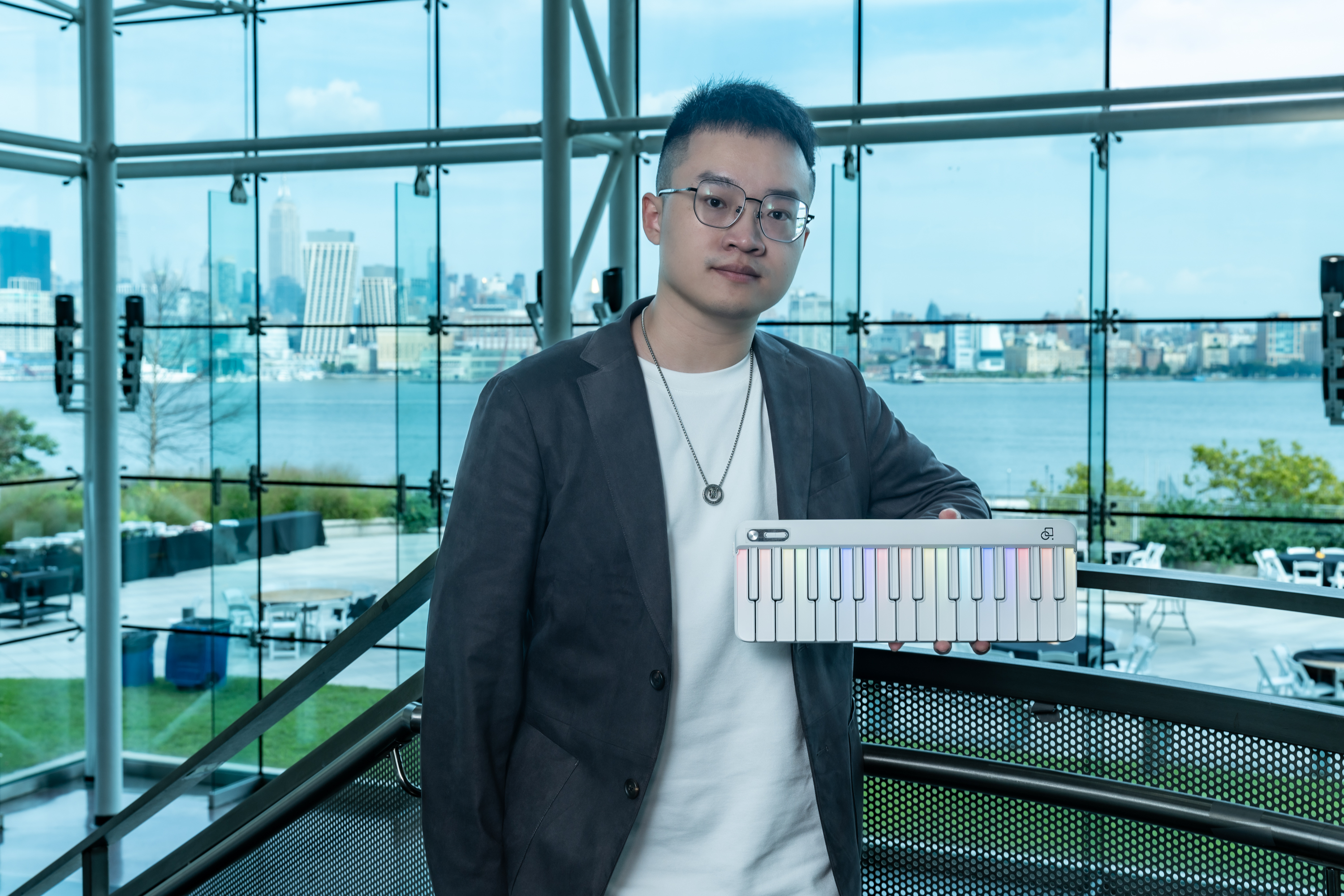Bohan Zhang stands holding his PopuPiano device with the New York City skyline in the background.