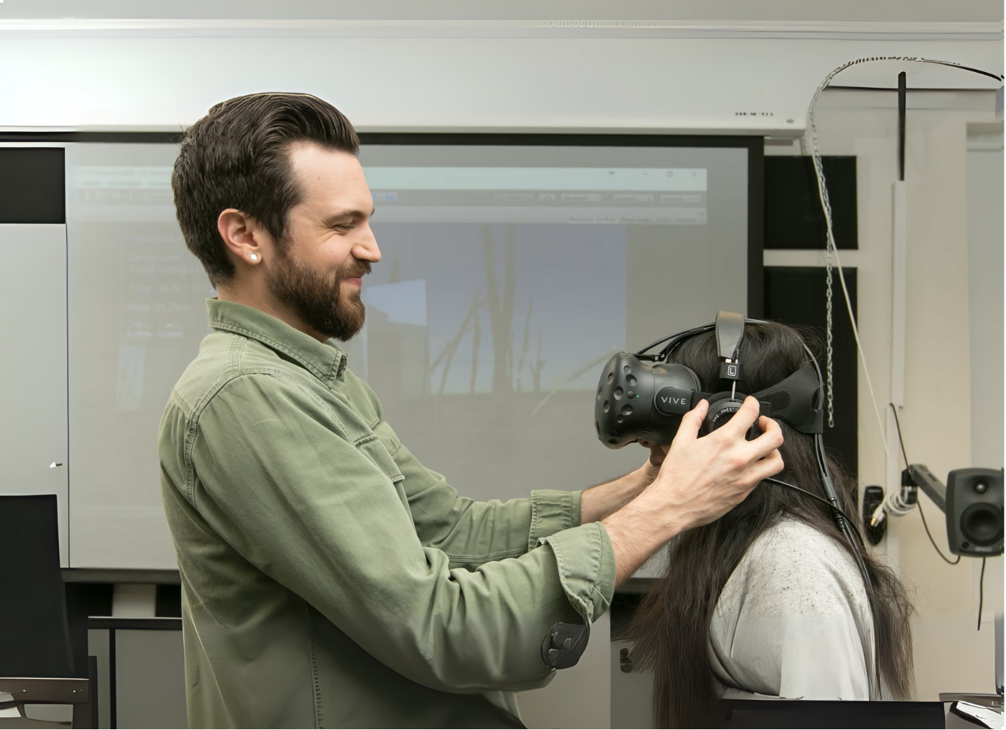 Tall male securing a virtual reality mask on a short female student.