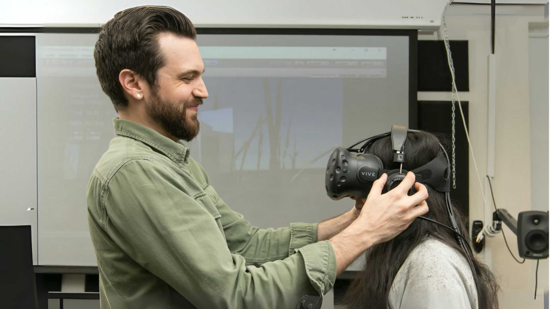 Tall male securing a virtual reality mask on a short female student.