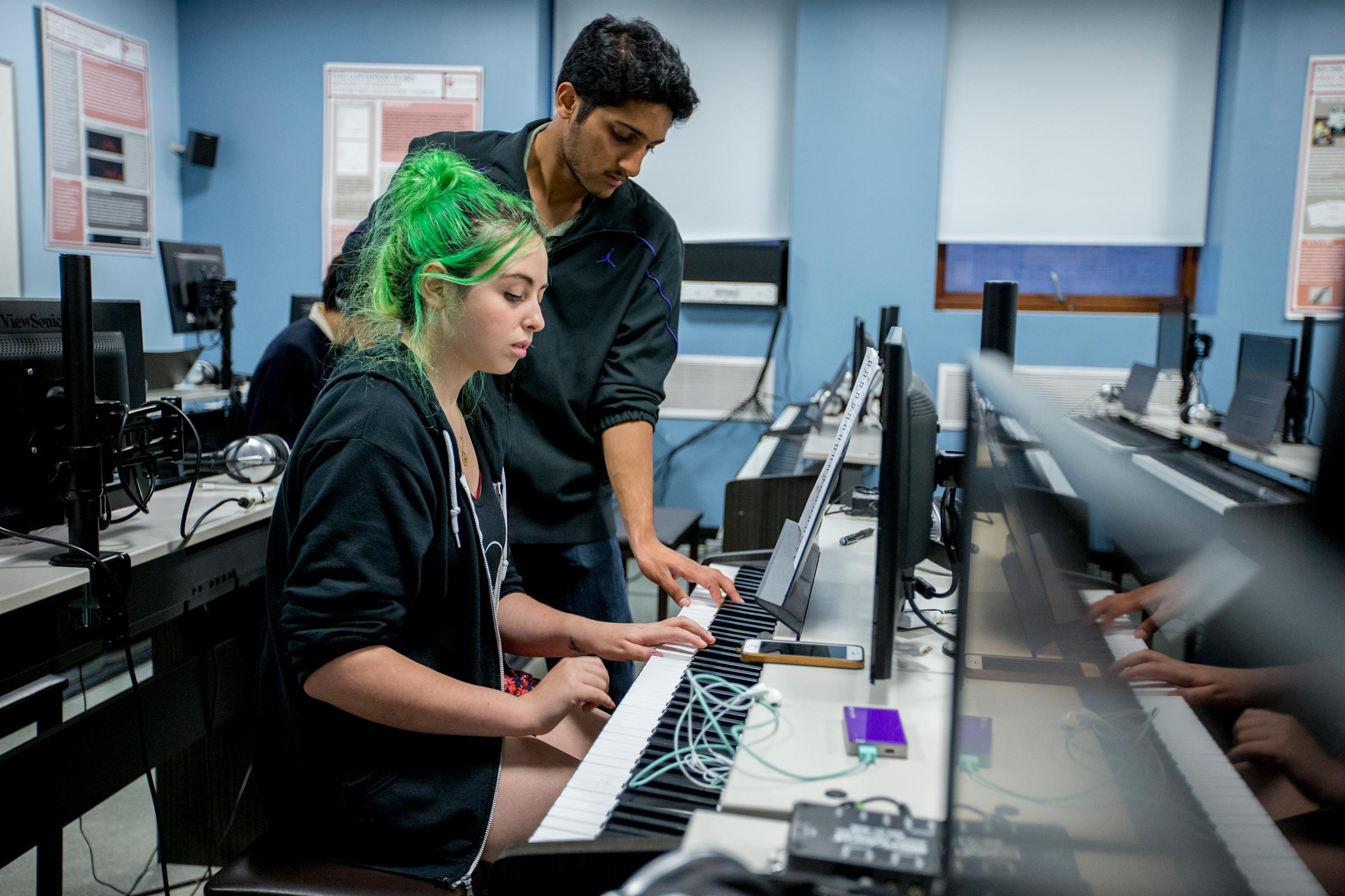 Two students work on a musical keyboard and computer set up.