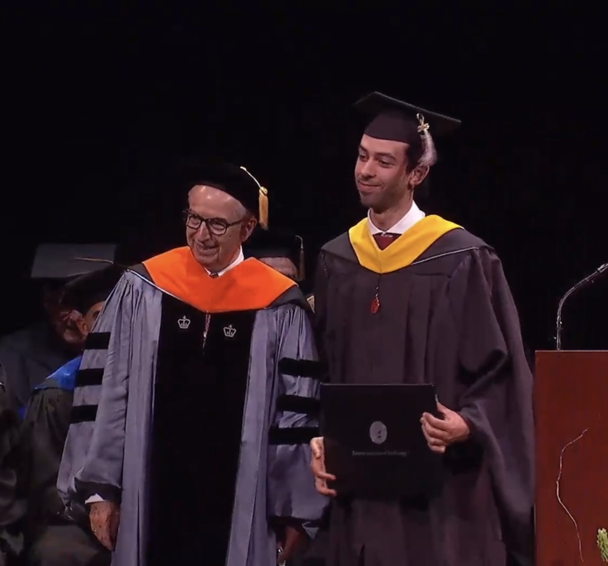 Dean Gregory Prastacos and Ahmed Ouerghemi pose for a photo at graduation. Ahmed is holding his diploma. 