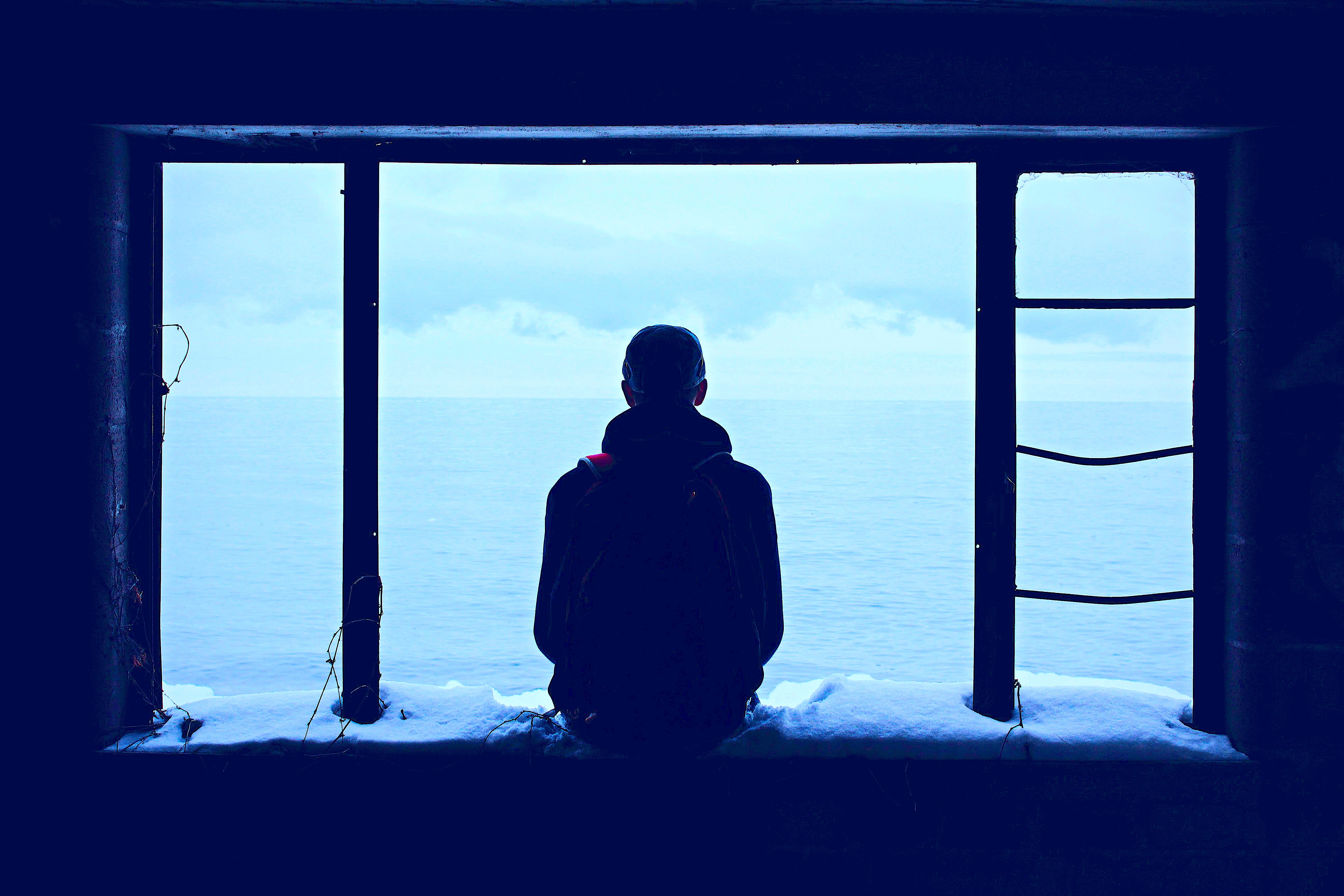 Silhouette of man staring out open window onto ocean, signifying loneliness