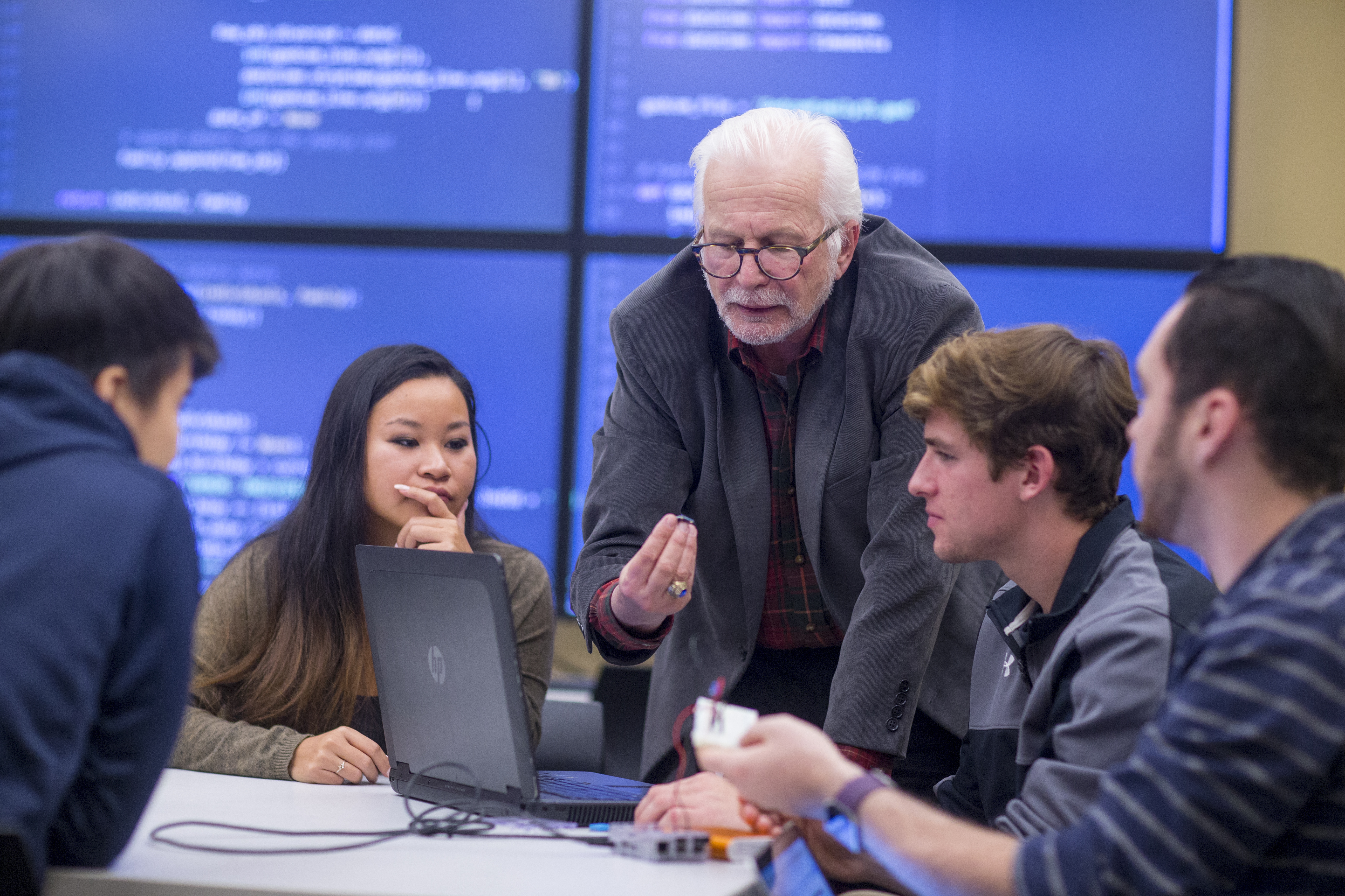 Students surrounding a laptop and working with a professor 