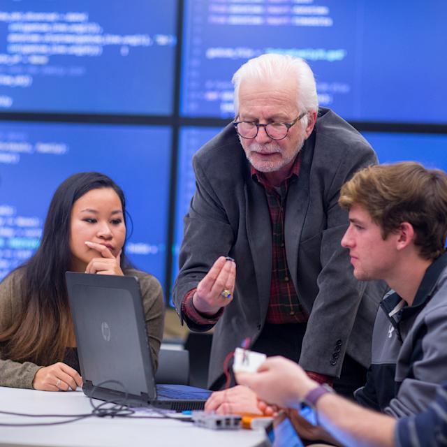 Students surrounding a laptop and working with a professor