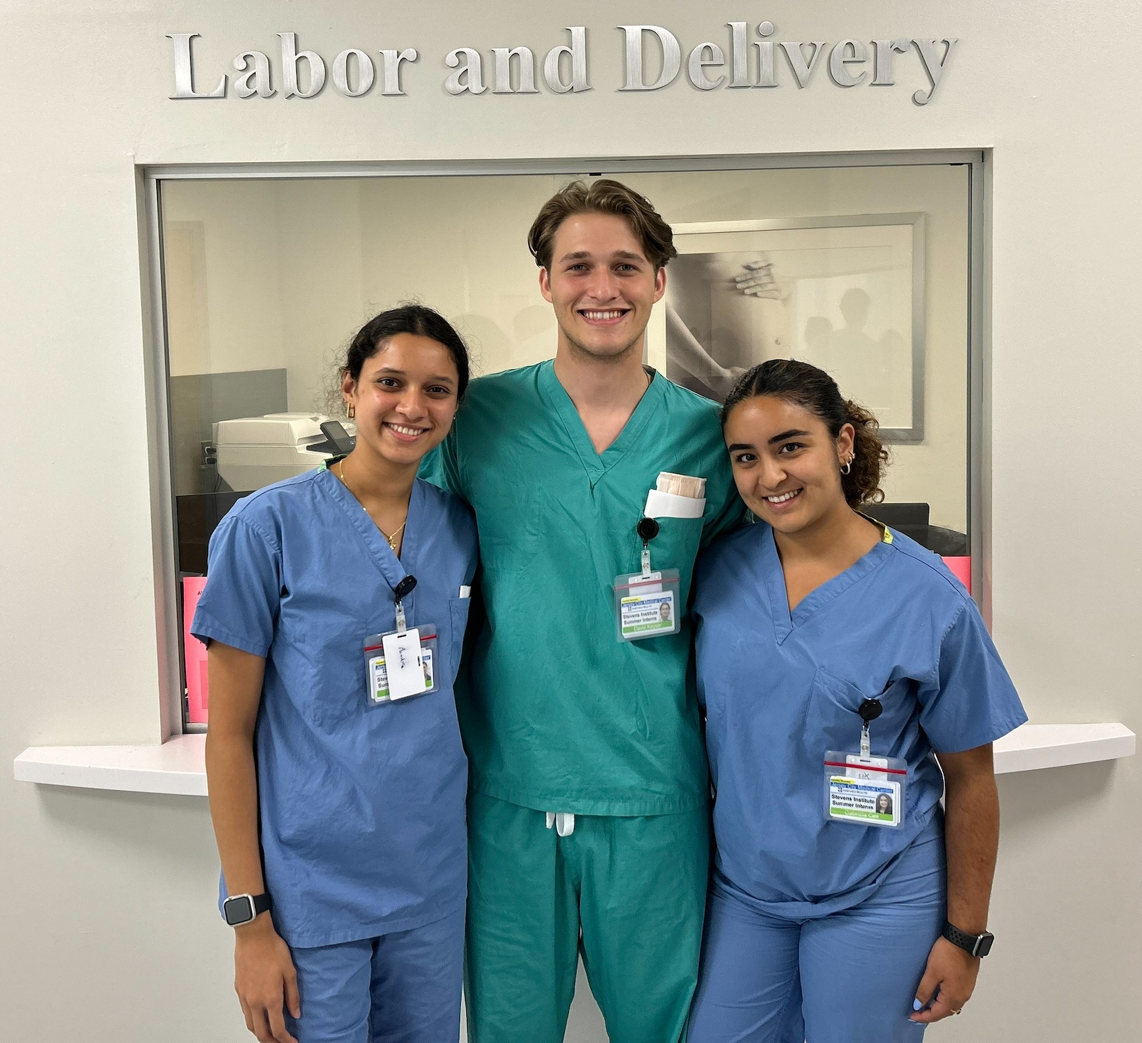 Three student OBGYN interns pose in front of a sign that reads Labor and Delivery.
