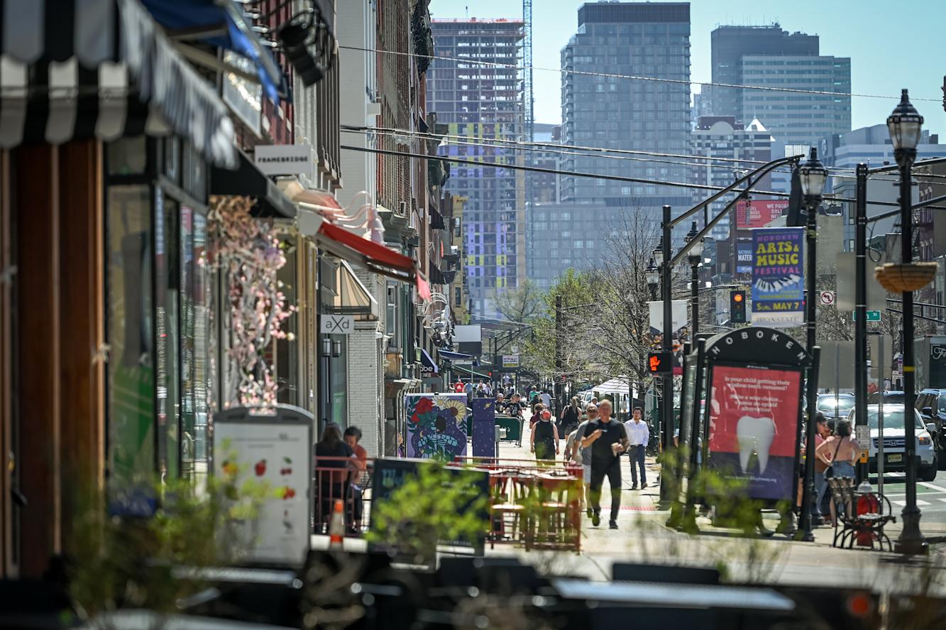 An image of businesses, people and traffic along Washington Street in Hoboken, NJ, with Manhattan in the background. 