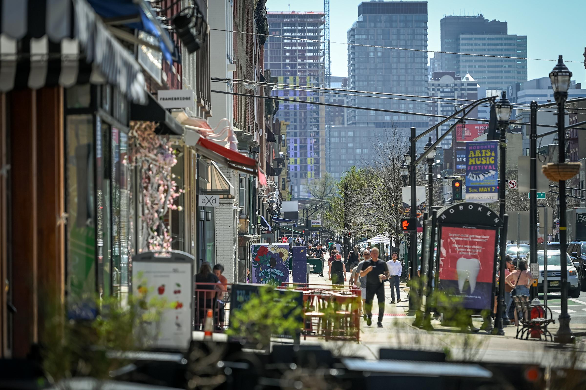 An image of businesses, people and traffic along Washington Street in Hoboken, NJ, with Manhattan in the background.