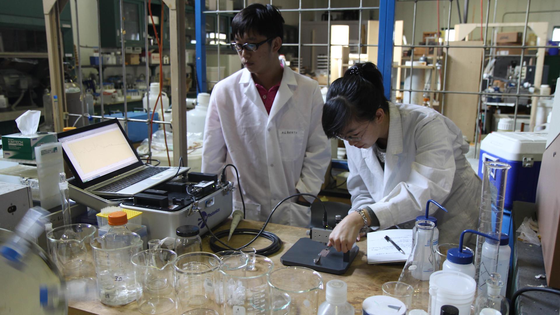 A student working with chemical equipment by a window showing the Empire State Building.