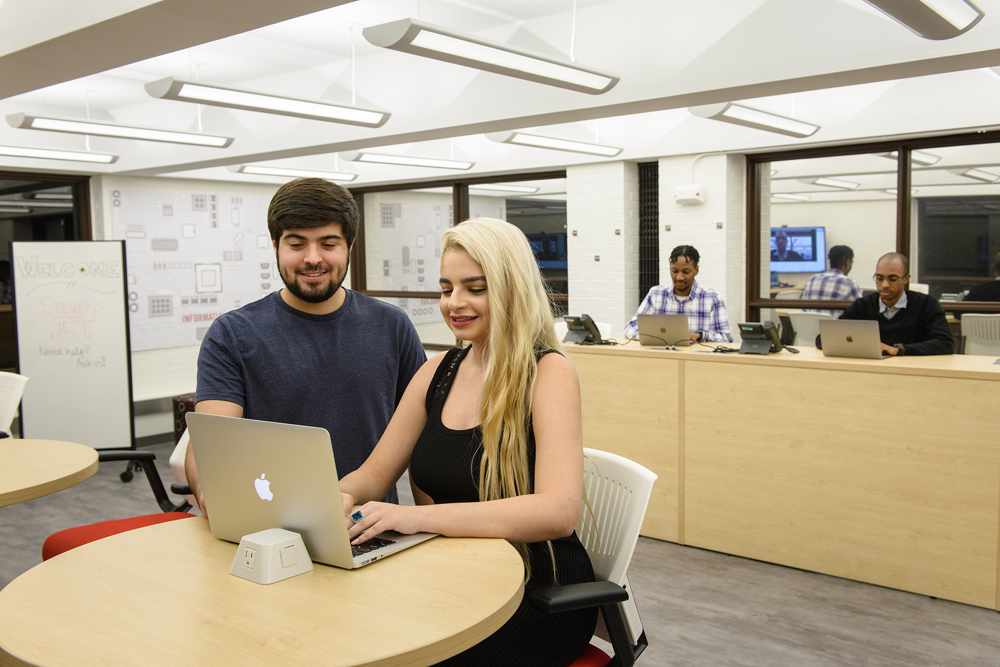 Two students looking at a laptop with IT staff in background