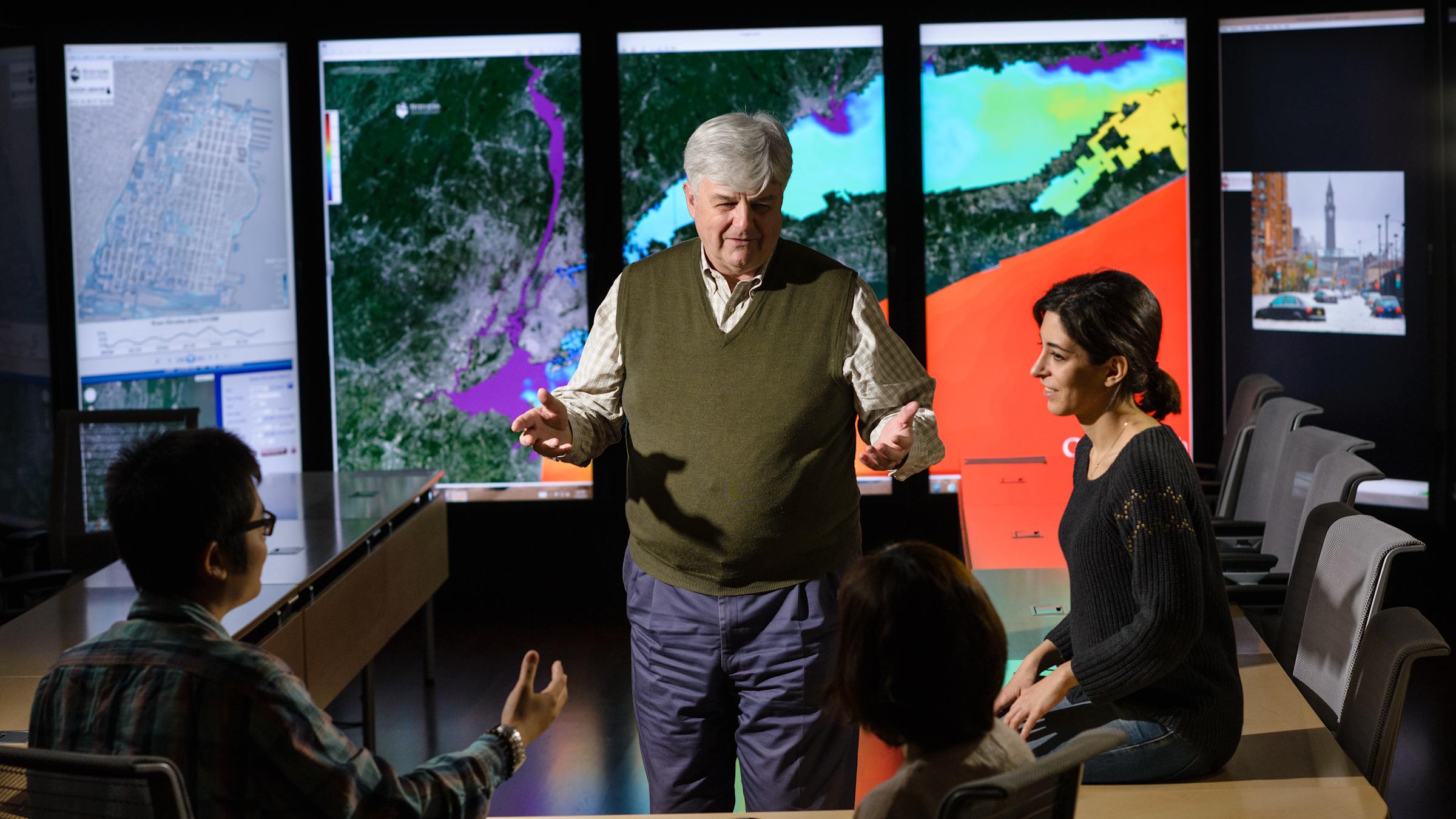 A professor in the immersion lab with satellite images of Hoboken and New York Harbor in the background