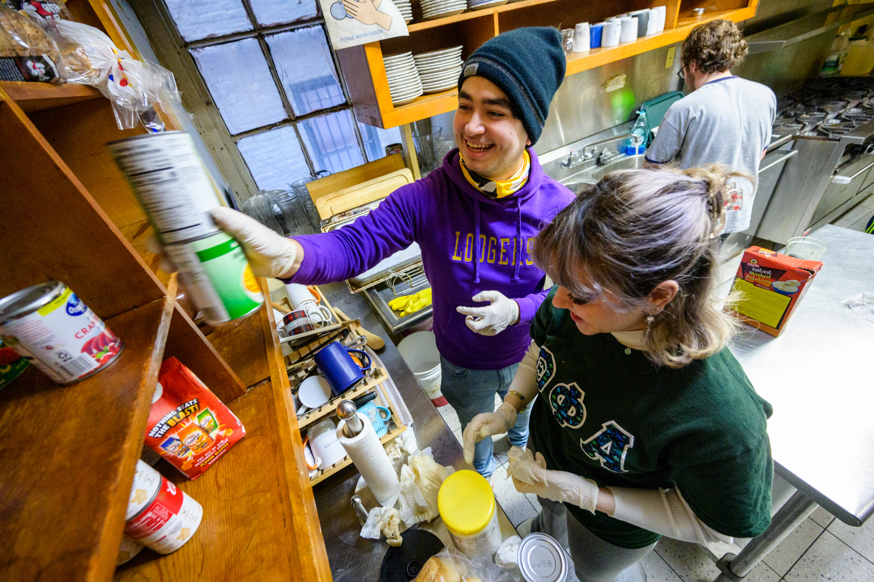 People putting cans of food into a kitchen cabinet